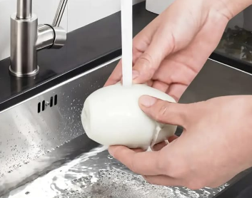 Person washing a white object under running water in a kitchen sink.